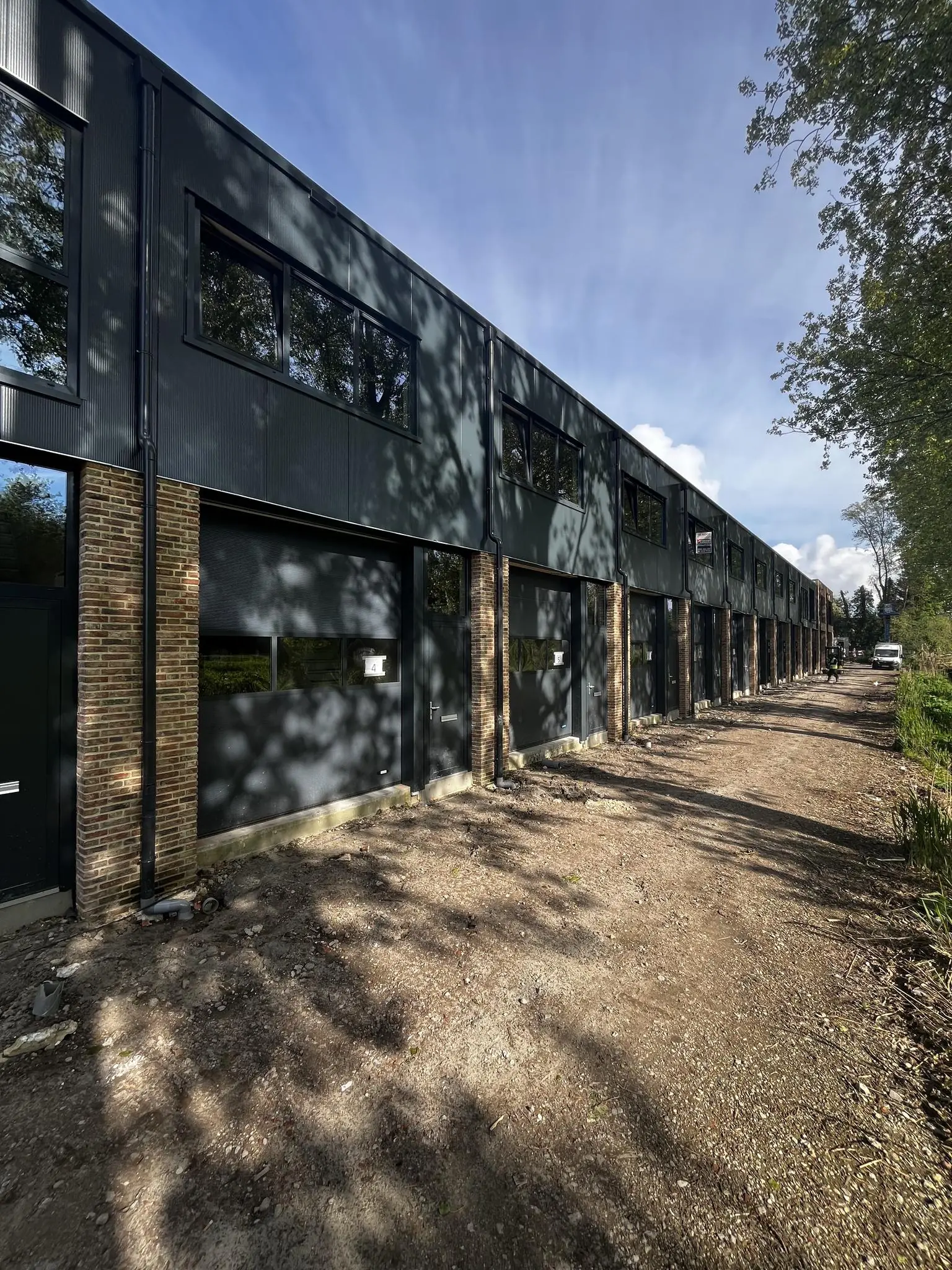 Nieuwbouw bedrijfsunits aan de Broekdijk West, gefotografeerd vanaf een onverharde weg op een zonnige dag.